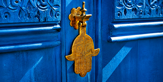 Hamsa hand door knocker in brass on a blue Moroccan door — protective symbols for the home, hamsa symbol of protection