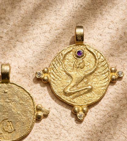 Gold winged goddess pendant with amethyst crown on sandstone, a protection talisman in relief
