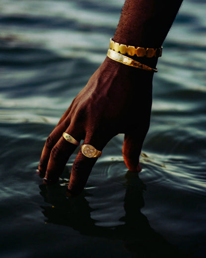 Hand dipped in seawater wearing gold boho rings and coin bracelets in sunlight