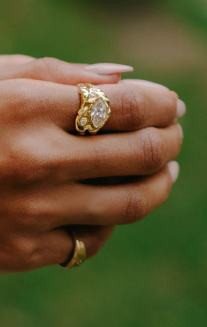 Yellow gold marquise engagement ring worn on hand outdoors, sculpted bezel catching light
