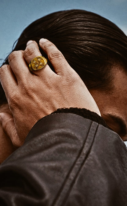 Mens signet ring in 18k gold worn with leather jacket, hand raised to hair